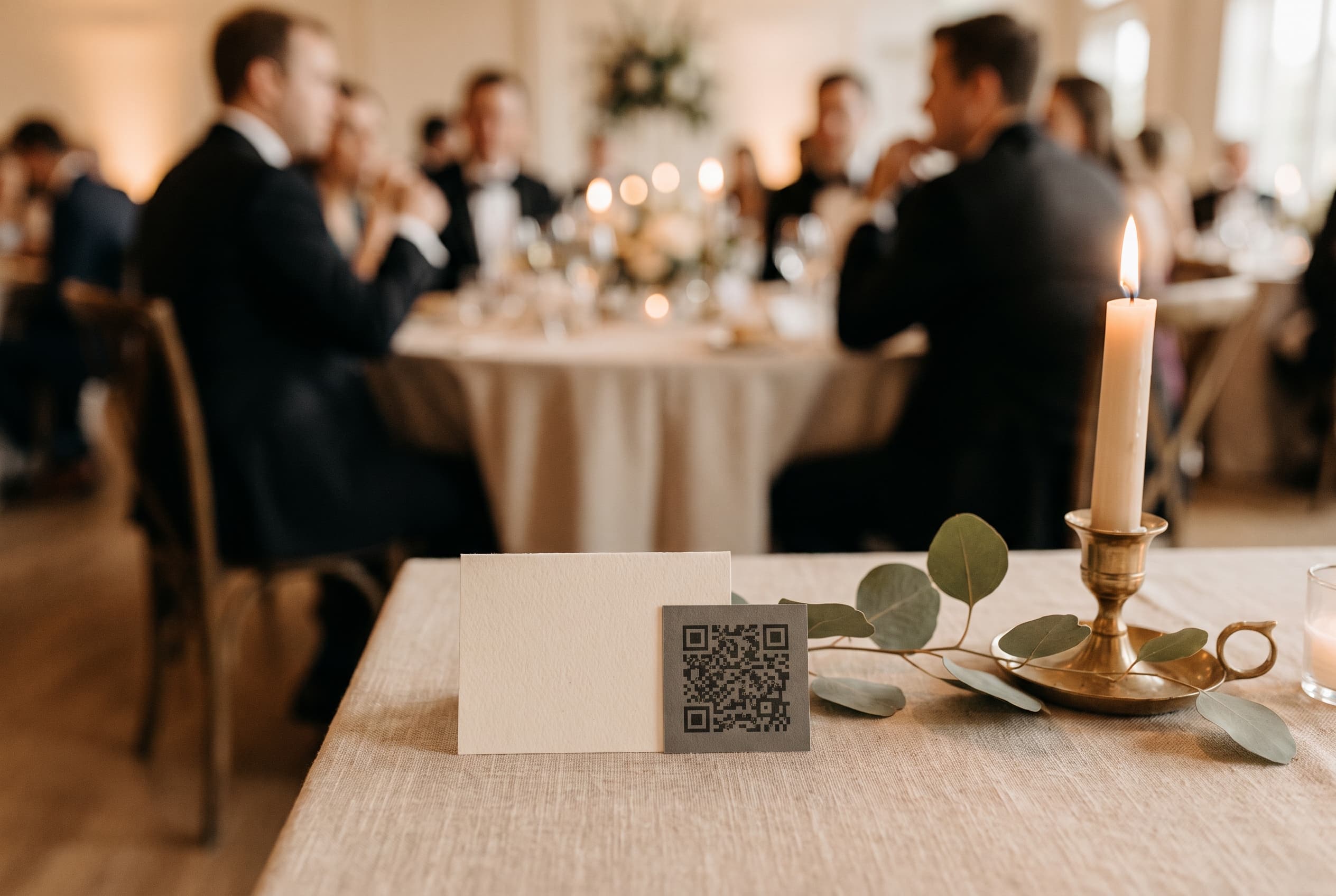 Carte imprimée avec un QR code élégant sur une table de réception de mariage, eucalyptus et bougie