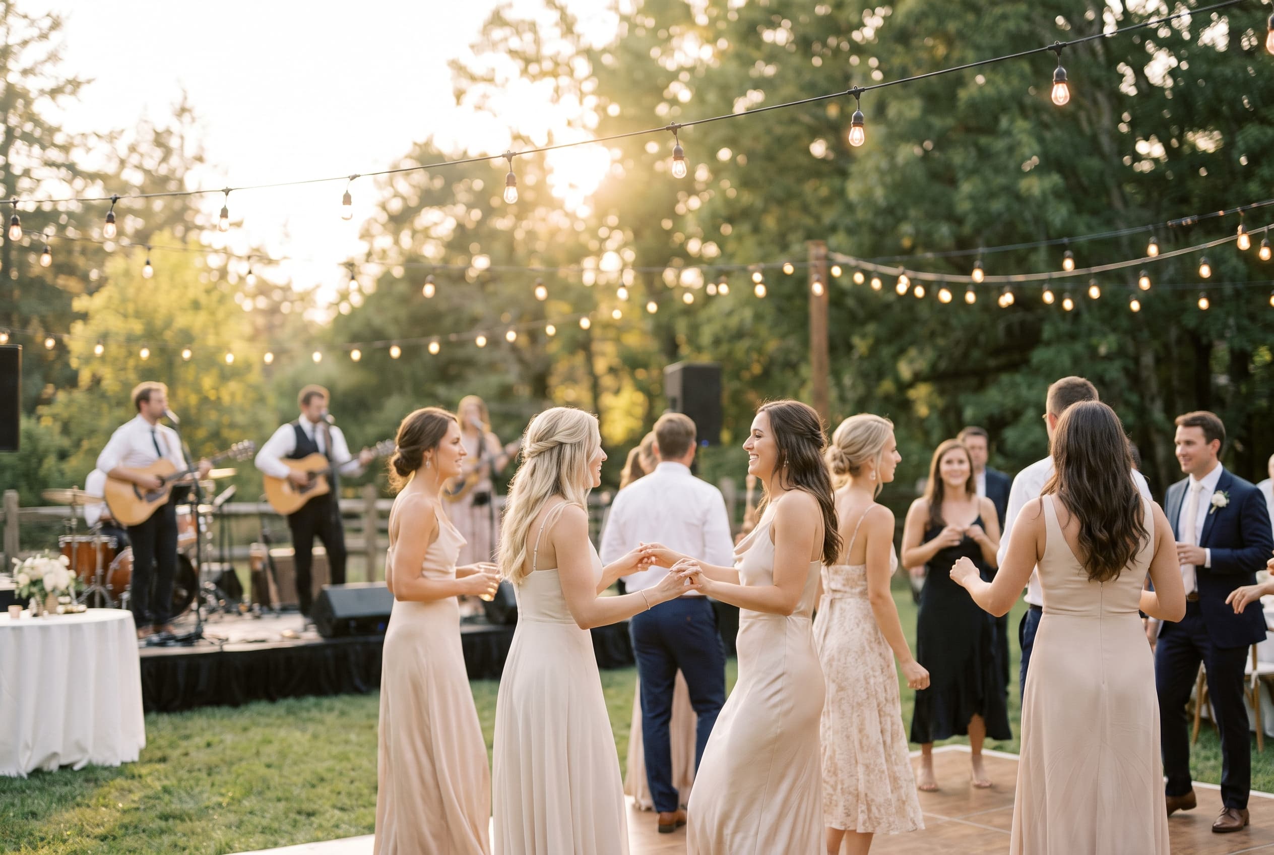 Invités dansant joyeusement sur une piste de danse extérieure à la lumière dorée du soir, guirlandes lumineuses au-dessus