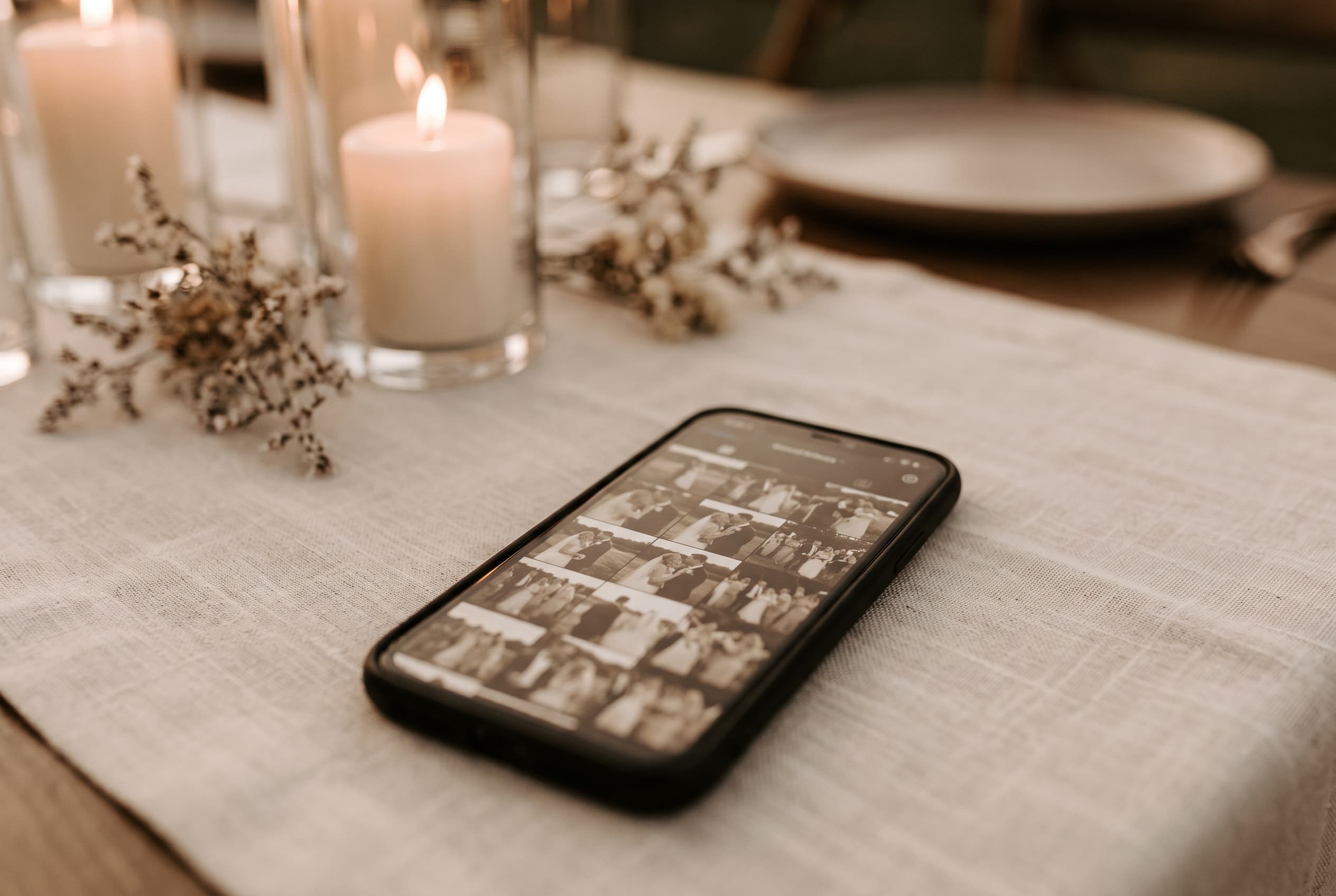 Smartphone posé sur une table de réception de mariage affichant une grille de photos en cours d'envoi, lumière dorée du soir