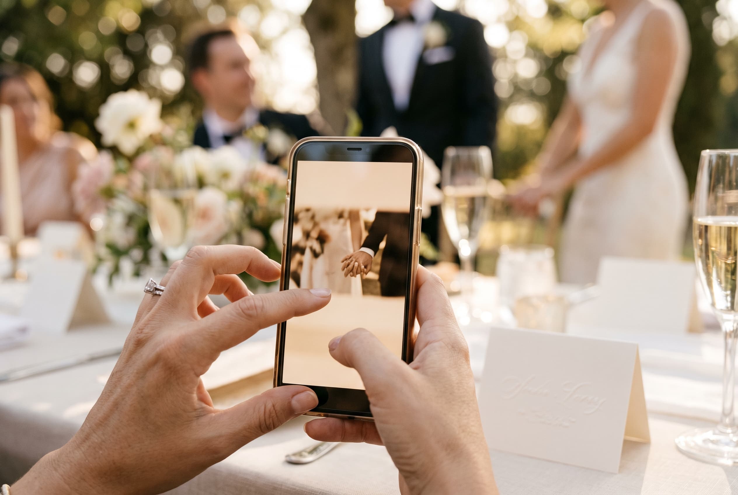 Main d'un invité de mariage tenant un smartphone, ambiance floue de réception en arrière-plan