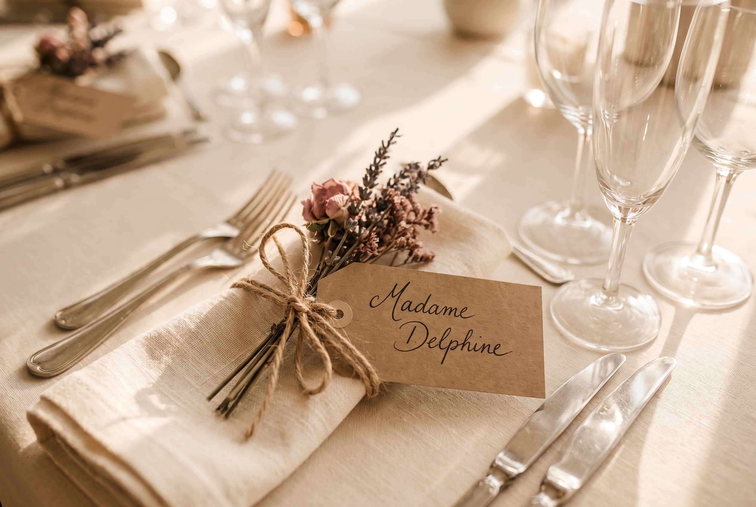 Marque-place de mariage en papier kraft calligraphié, noué avec de la ficelle et un brin de fleurs séchées, table de réception, lumière dorée du soir