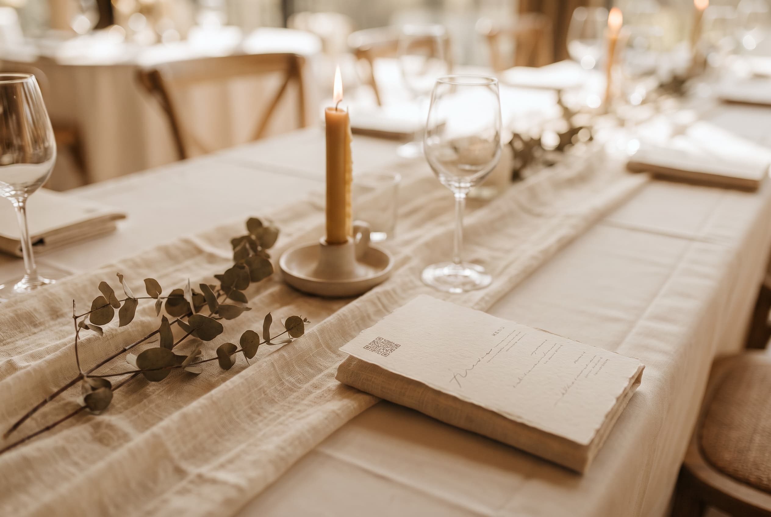 Menu de mariage avec un QR code et une ligne d'invitation, posé sur une table décorée d'eucalyptus et d'une bougie